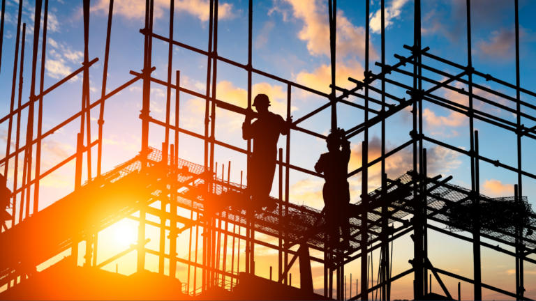 Fire Risks image construction site scaffolding in silhouette with two people standing on it. Sun is low in the sky, a firey orange to suggest fire risks.