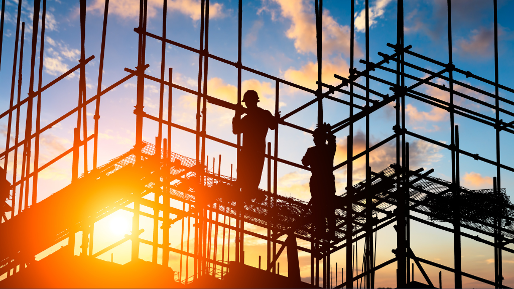 construction site scaffolding in silhouette with two people standing on it. Sun is low in the sky, a firey orange to suggest fire risks.